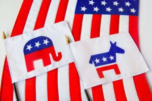 Republican-Elephant-and-Democratic-Donkey-political-party-symbols-on-two-small-flags-laying-on-the-American-Flag-GettyImages-1167212213_KSedit_FT A close up of the republican and democrat symbols on a flag.